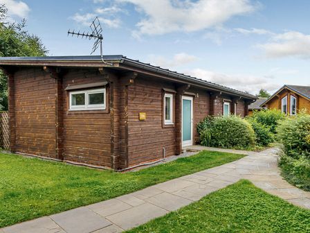 A wooden cabin with a pathway and greenery at Chestnut Spa in Carlton Miniott near Thirsk
