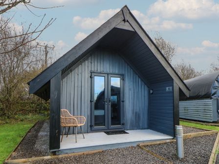 A cabin with an entrance door and chair at Garden Lodge 6 in Swansea