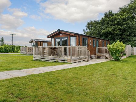 A log cabin with decking and a pathway at Alder Spa Carlton Miniott near Thirsk