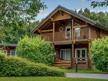 A wooden house with a balcony and shrubs at Birch Spa in Carlton Miniott near Thirsk