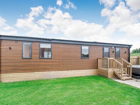 A wooden cabin exterior with grass and steps at Cedar Spa in Carlton Miniott near Thirsk