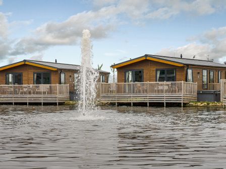 Two lodges with decks by a water fountain at Oak Waterside Spa Carlton Miniott near Thirsk