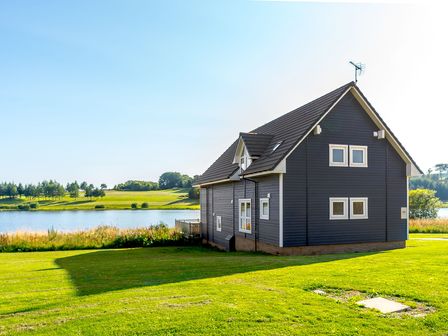 A house by a lake with grass and trees at Lochside Premier Spa (Pet) in Dundee