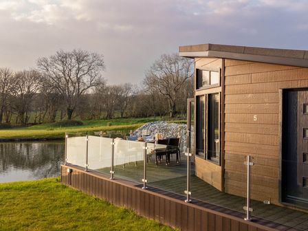 An outdoor deck with a table and chairs beside a lake at Lake View Spa in Praze-An-Beeble