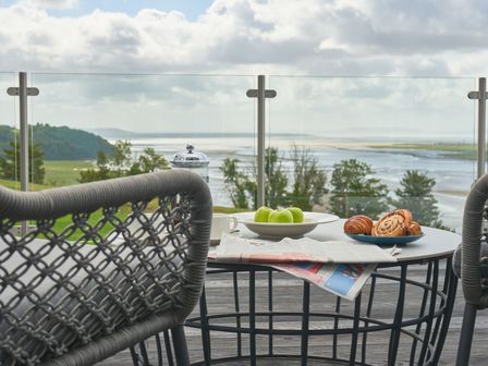An outdoor area with a table and chairs overlooking a river at Milk Wood 3 Spa in Laugharne