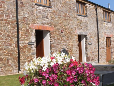 An outdoor view of stone buildings with doors and a flower pot at Westcotts in Marhamchurch