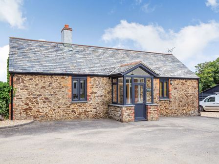 The exterior of a stone cottage with a parking area at Godolphin Stable Bude