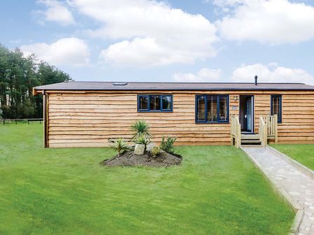 A wooden cabin with windows and a pathway at Lancaster Lodge in Fair Oak