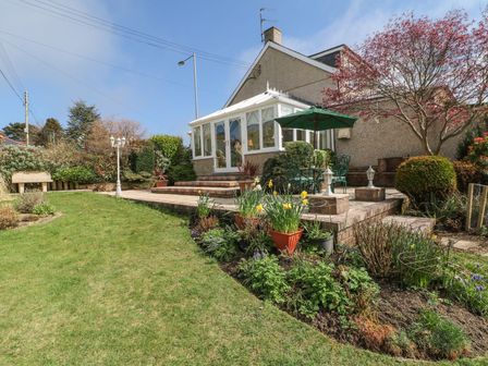A garden with a conservatory and seating area at Llwyn Derw in Talybont