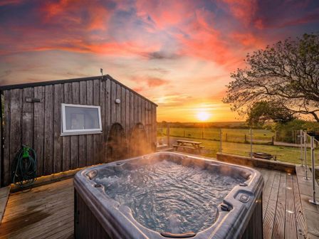 A hot tub next to a wooden building during sunset at The lodge at Plumstone View in Letterston