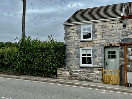 A stone house with a hedge and street at Penderyn Cottage Aberdare
