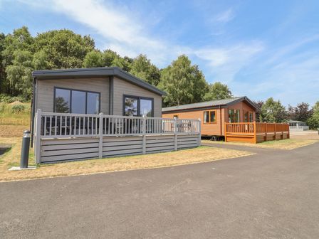 Two cabins with decking and trees at Cedar Lodge 3 Bedrooms Delamere