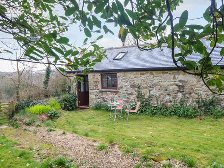 A garden with a stone building and seating area at Little Tregarrick in Helston