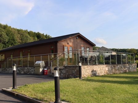 An outdoor view of a lodge with a deck and barbecue at Holly Lodge in Lloc near Caerwys
