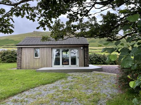 A cabin with a stone wall and sliding door at The Faithfuls Cabin in Dingle, County Kerry