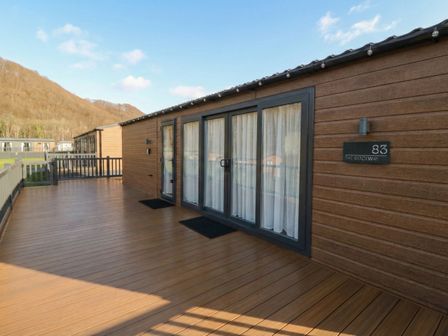A wooden deck with sliding doors and curtains at The Ridgeway in New Quay