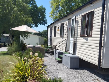 An outdoor area with a caravan, chairs, and an umbrella at Llanarmon-yn-Ial Mold 3-Bed Caravan, Sleeps 6 Llanarmon-Yn-Ial