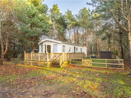 A mobile home with a wooden deck and trees at Sprindrift - Kelling Heath Holiday Park in Holt