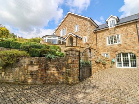 An exterior view of a house with stone walls and landscaped garden at Stone Lodge near Haltwhistle