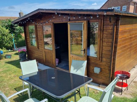 A garden shed with a table and chairs in the garden at tbc 
