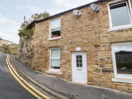 Stone wall cottage with white door and windows on a sloped street with double yellow lines at Bridge Cottage in Haltwhistle near Hadrians Wall