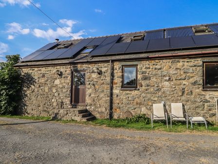 An outdoor view of a stone building with solar panels and chairs at Pandy Farmhouse