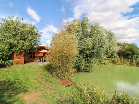 A lodge and pond surrounded by grass and trees at Willow Lodge Stowmarket