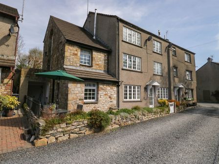 A stone and stucco residential building with multiple windows and doors and a green umbrella over a patio area at The Old Mill in Cark in Cartmel