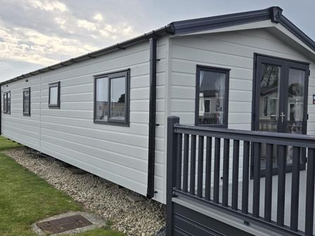 A mobile home with a deck and windows at 3 Bedroom Cabin Sleeps 6 - Shared Pool & Shared Hot Tub, Flamingo Land Resort near Malton