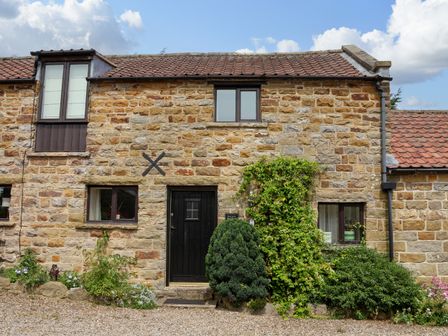 Stone cottage with black door and windows with plants in front at Hayloft Cottage in Staintondale
