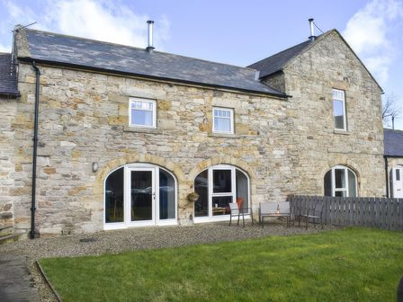 A garden with a stone wall house and outdoor furniture at The Hayloft in Hexham