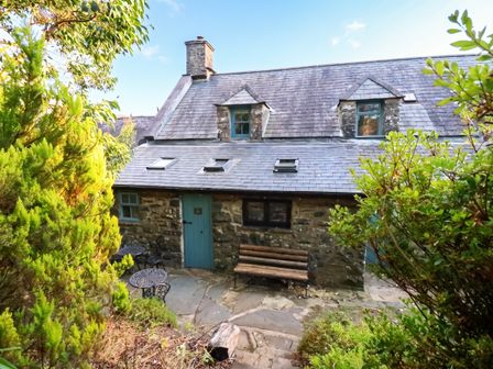 A cottage with a bench and table surrounded by greenery at Y Cwtch in Dolgellau