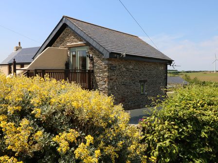 A stone house with a deck and flowering plants at Oak Cottage in Truro