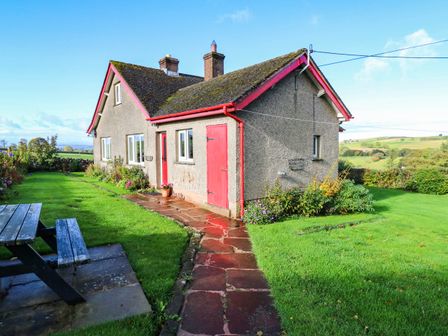 A house with a red door and windows surrounded by grass at The Bungalow in Penrith