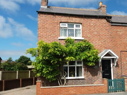 A brick house with white windows and a black door covered with green vines at Sunnyside Cottage Muston near Filey