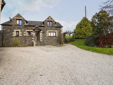 A house with a gravel driveway and garden at High Beck Cottage in Kendal