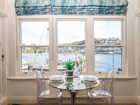A dining area with a table and chairs overlooking the sea at 1 Embankment House in Dartmouth