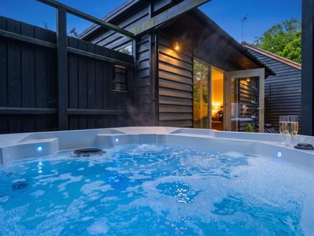 A hot tub with steam and two glasses near a building in a garden