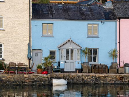 A house with table and chairs by the water at Quay Cottage in