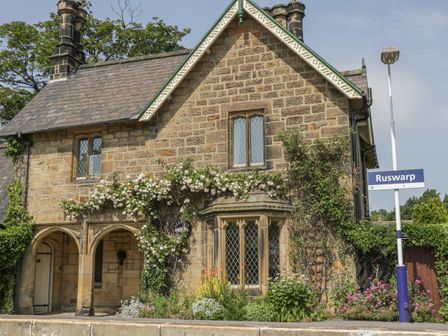 A stone house with arched doorway and climbing plants near a Ruswarp sign at The Station House Ruswarp near Whitby