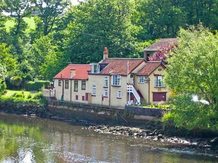A house with red roof tiles beside a river surrounded by trees at Waterloo Cottage Annexe Ruswarp near Whitby