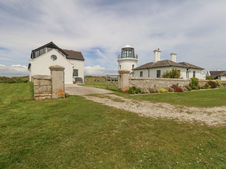 A lighthouse and white buildings with a stone wall and grassy area at Old Higher Lighthouse Branscombe Lodge Portland Bill
