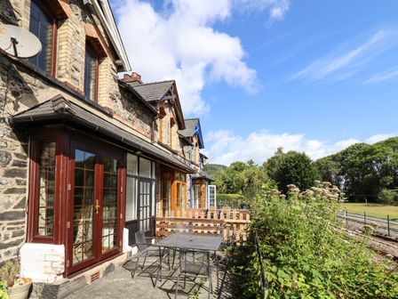 Exterior view of stone cottages with outdoor tables and chairs near railway tracks at 3 Railway Cottages in Betws-y-Coed