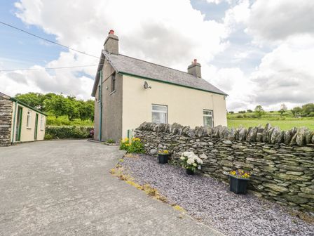 A two chimney house with a stone wall and potted flowers in a rural setting at Penrhyddion Ucha in Capel Garmon near Betws-y-Coed