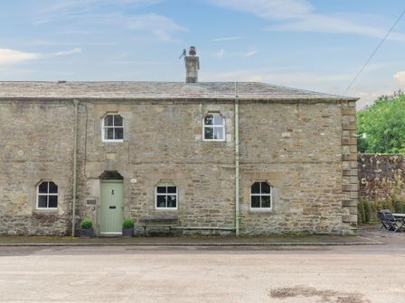 Stone house with green door and multiple windows by a street with outdoor table and chairs at Reiver's Rest in Hesleyside near Bellingham