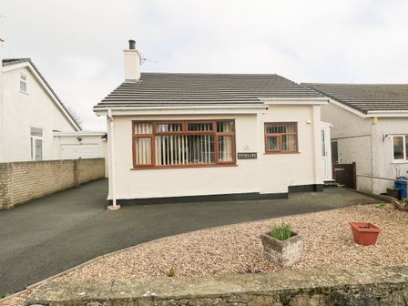 A single-story house with a driveway and pebble garden at Penelope in Benllech near Red Wharf Bay