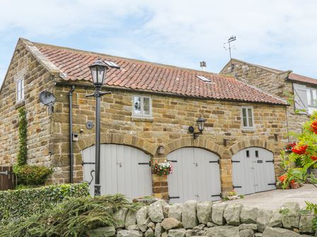 A stone building with three arched gray doors and a tiled roof with windows at The Loft in Staintondale