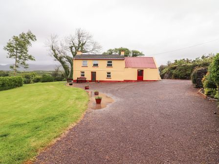 A yellow house with red doors and a gravel driveway surrounded by greenery at Ceol Na N'ean in Sneem County Kerry