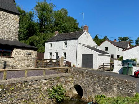 A white house with a garage next to a stone bridge over a small stream at Bwthyn Y Felin Star in Cardigan