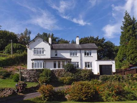A two story white house with a garage surrounded by greenery and trees at Llechwedd in Dolgellau